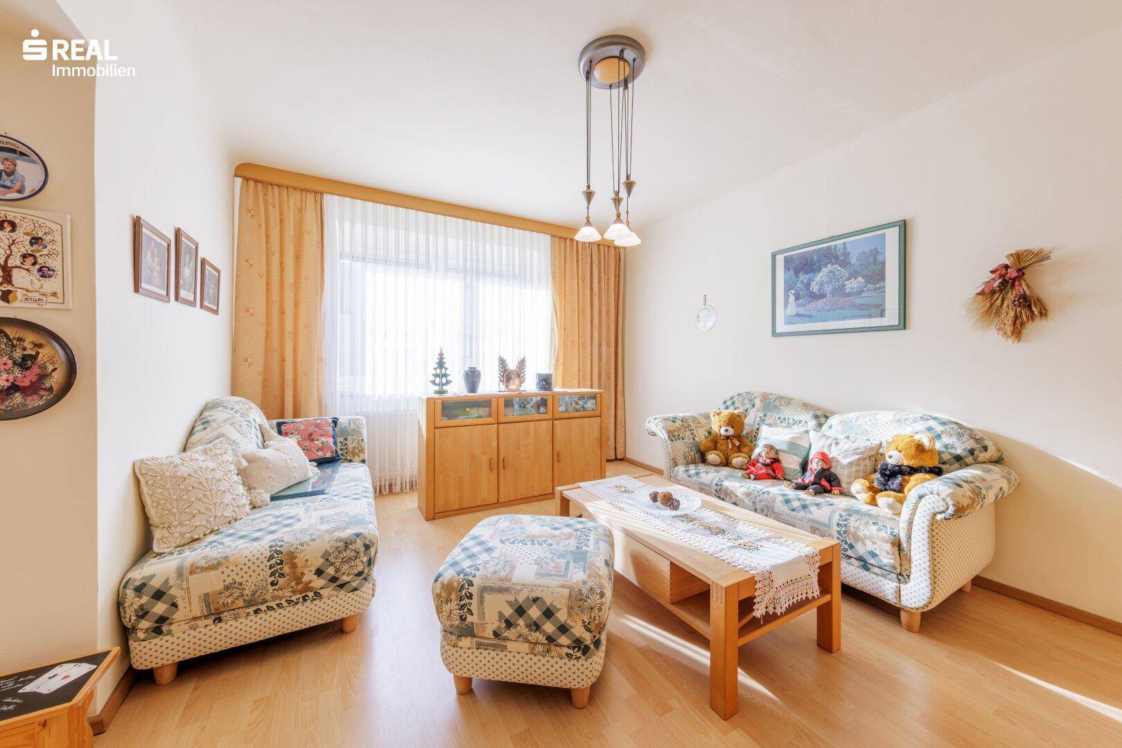 Wohnzimmer mit bequemen Sofas, Couchtisch und Laminatboden, hell durch große Fenster.