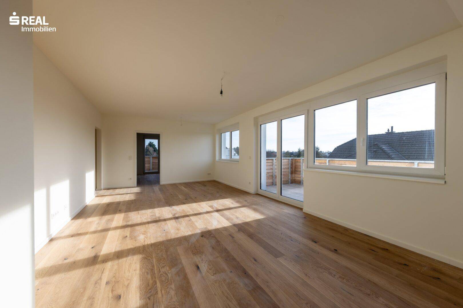 Heller, leerer Wohnraum mit Eichenparkettboden und Zugang zu einem Balkon oder einer Terrasse.
