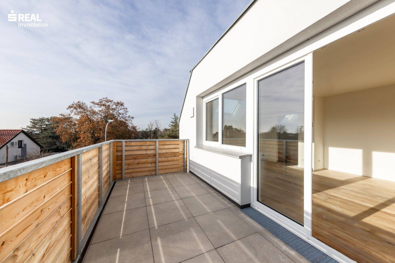 Geräumiger Balkon mit Holzgeländer, Fliesenboden und weitem Blick über die Umgebung.