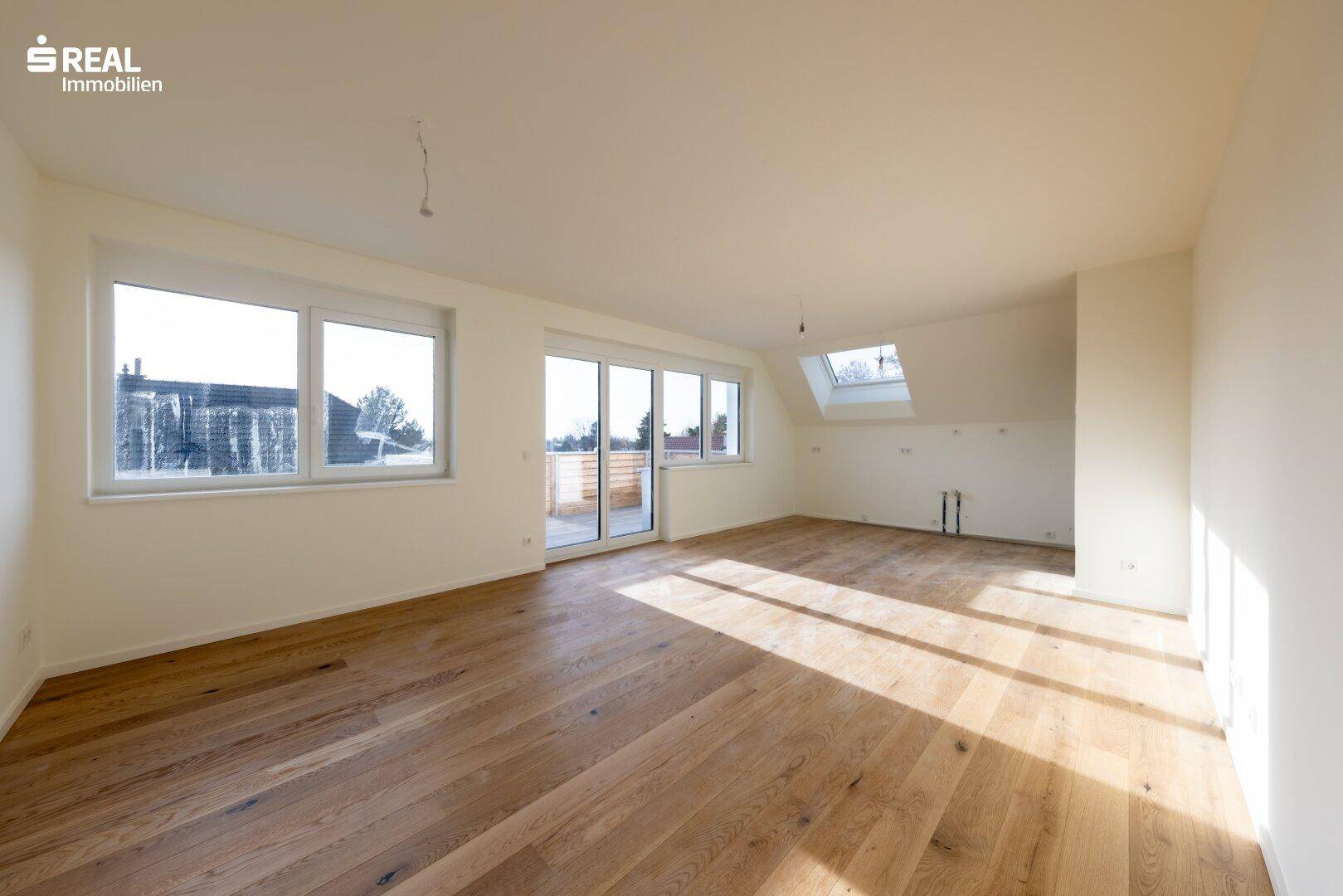 Lichtdurchfluteter Wohnbereich mit Holzboden, großen Fenstern und einem Dachfenster.