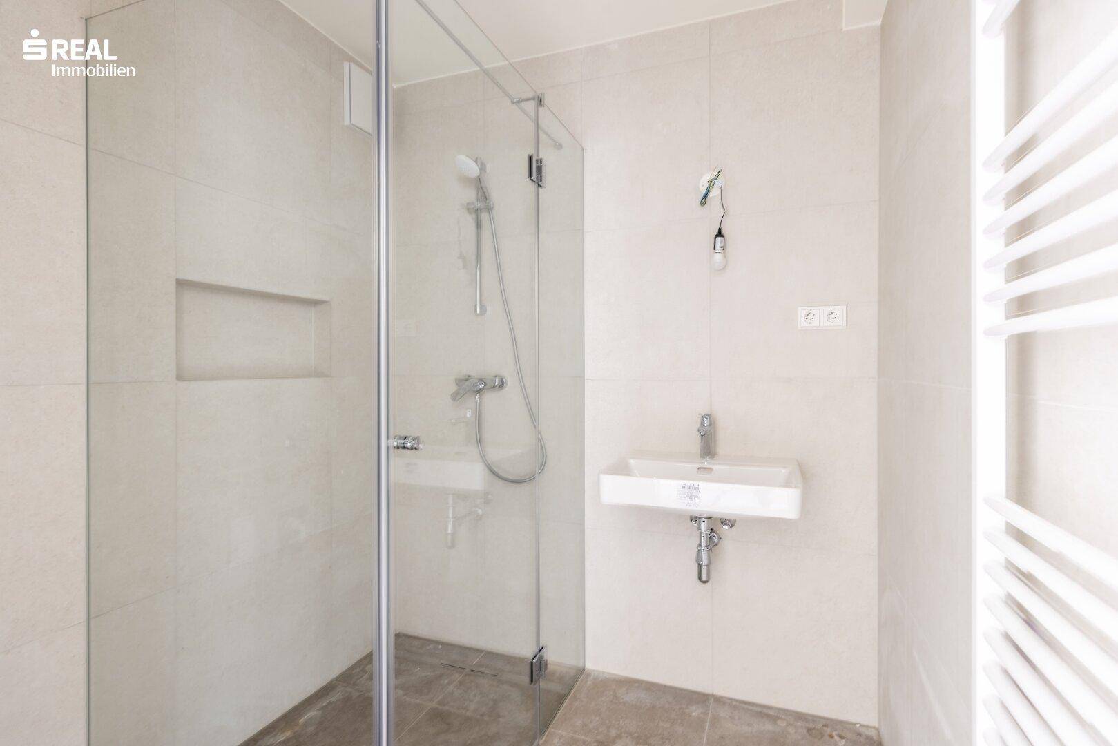 Helles Badezimmer mit moderner Dusche, Einzelwaschbecken und Fliesen an Wänden und Boden.