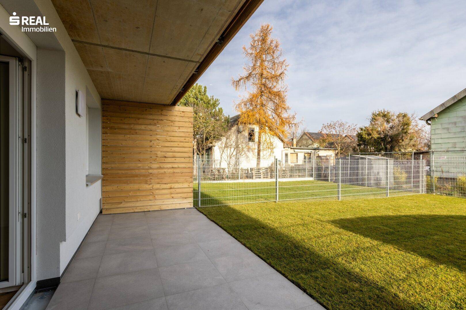 Geflieste Terrasse im Erdgeschoss mit Holzabtrennung und direktem Zugang zum privaten Garten.