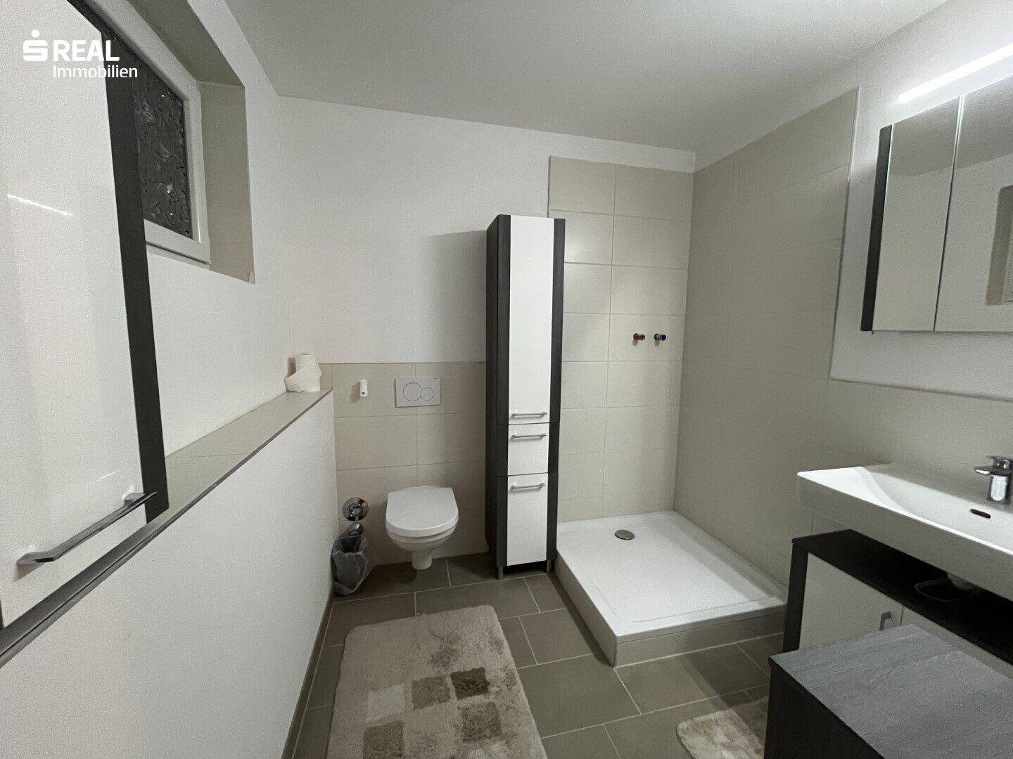 Modernes Badezimmer mit ebenerdiger Dusche, wandhängendem WC und Fenster für Tageslicht.