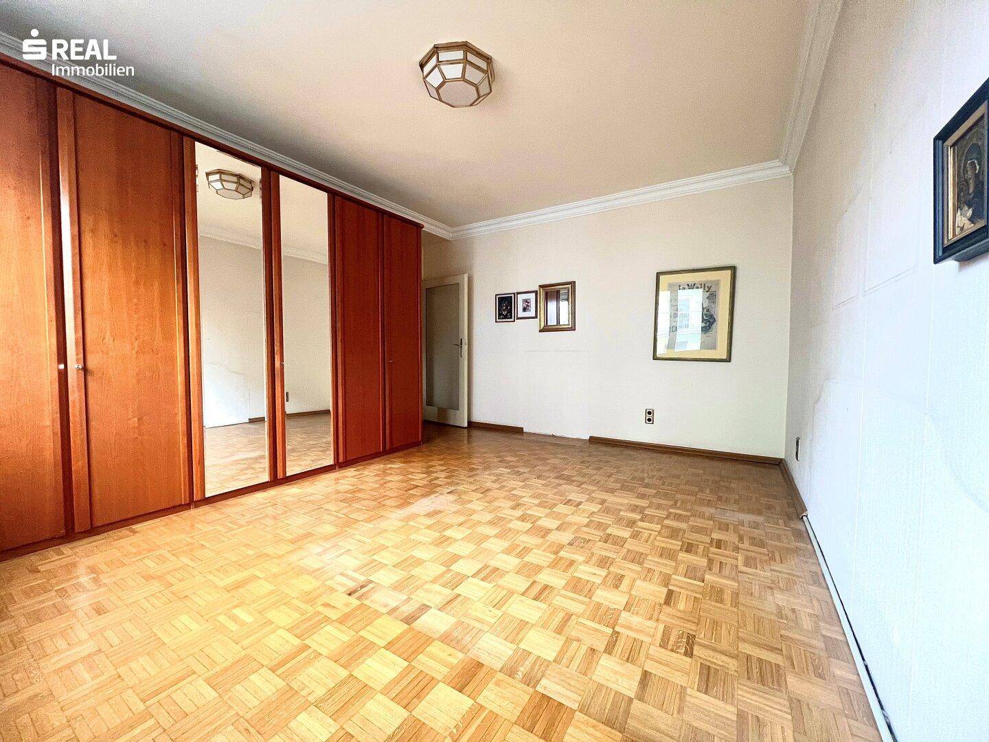 Helles Schlafzimmer mit Parkettboden und einem großen Spiegelschrank.