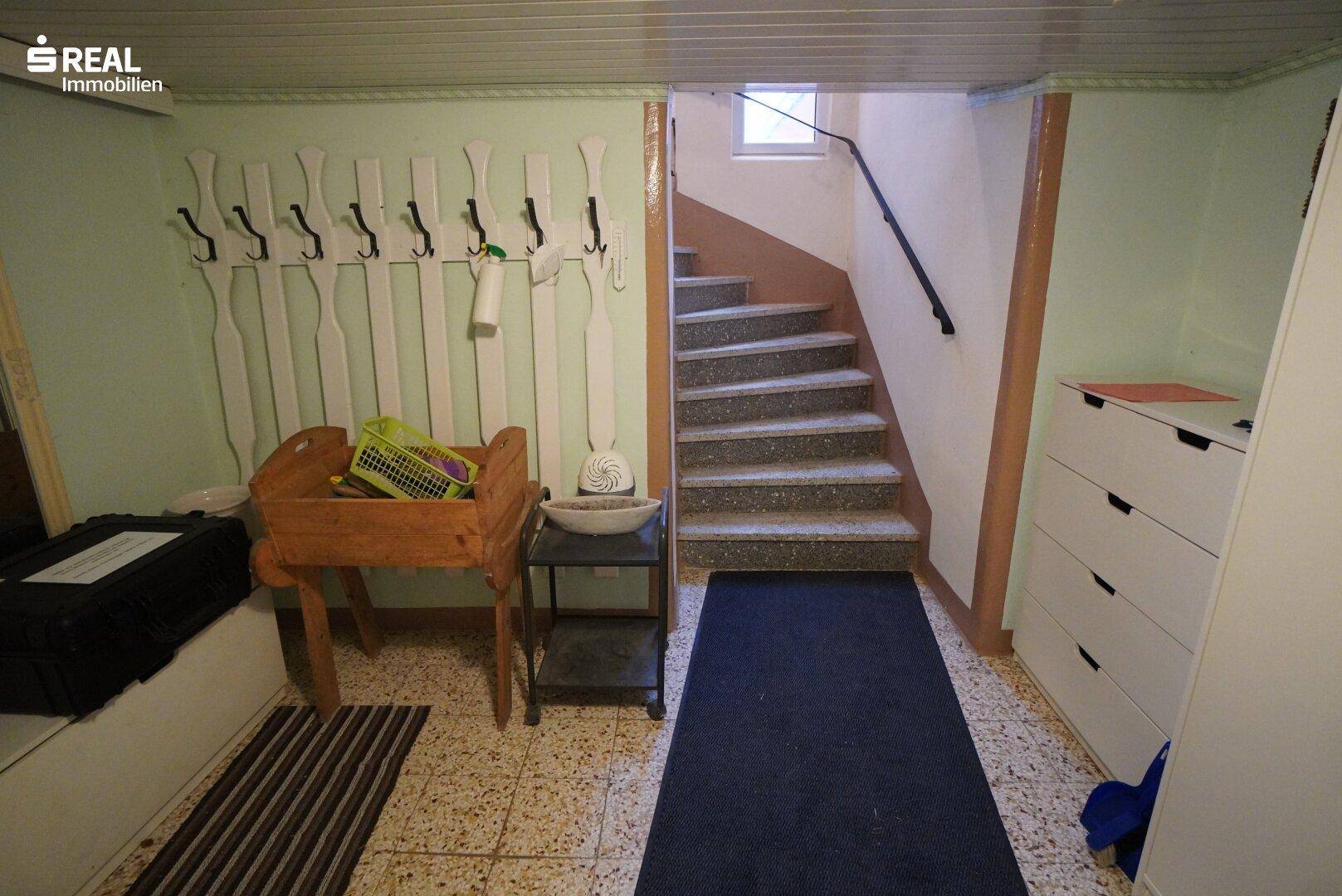 Flur mit Terrazzoboden, Garderobe und Treppe zum Obergeschoss.