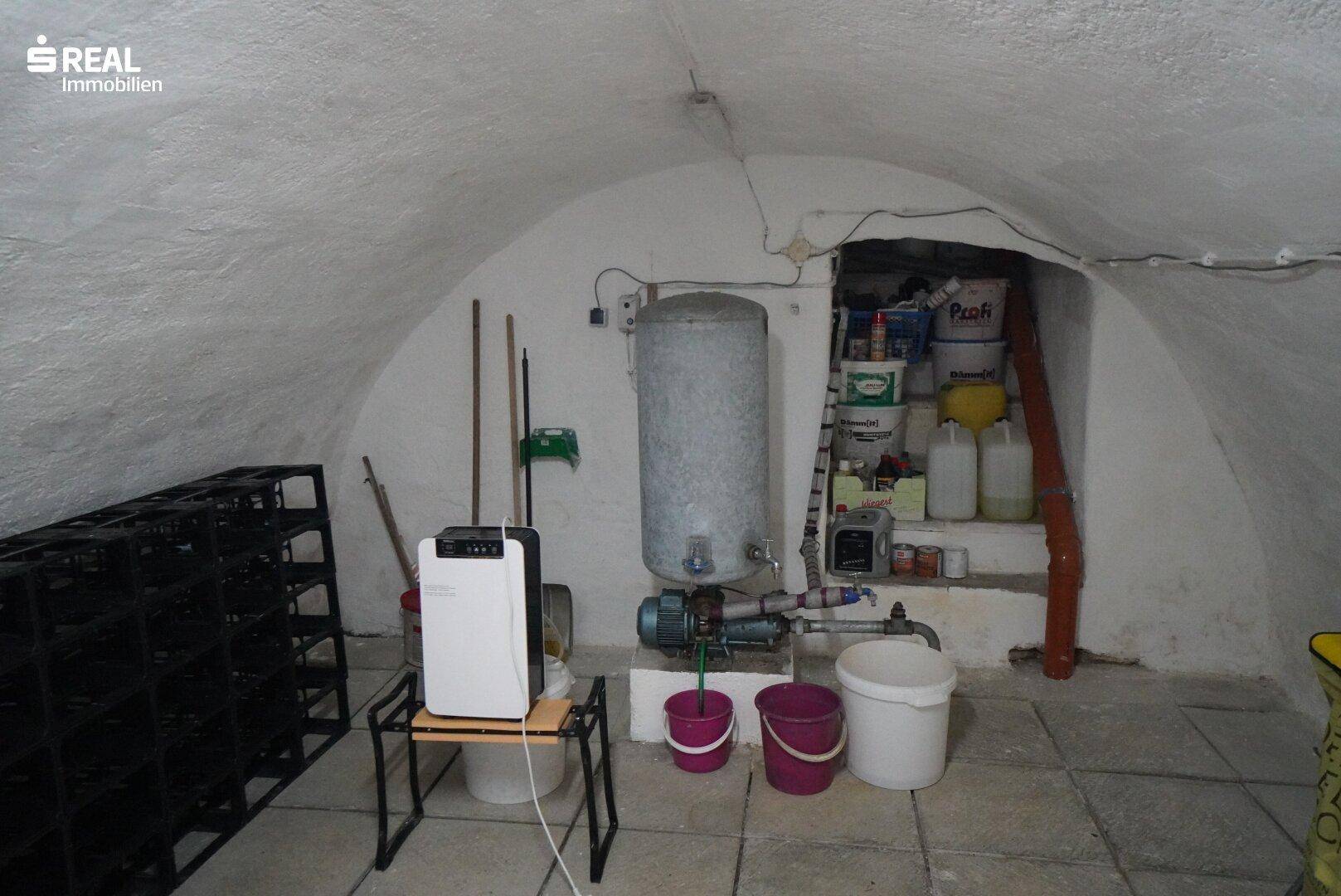 Gewölbekeller mit Lagerregalen, Wasserboiler und verschiedenen Haushaltsgegenständen.