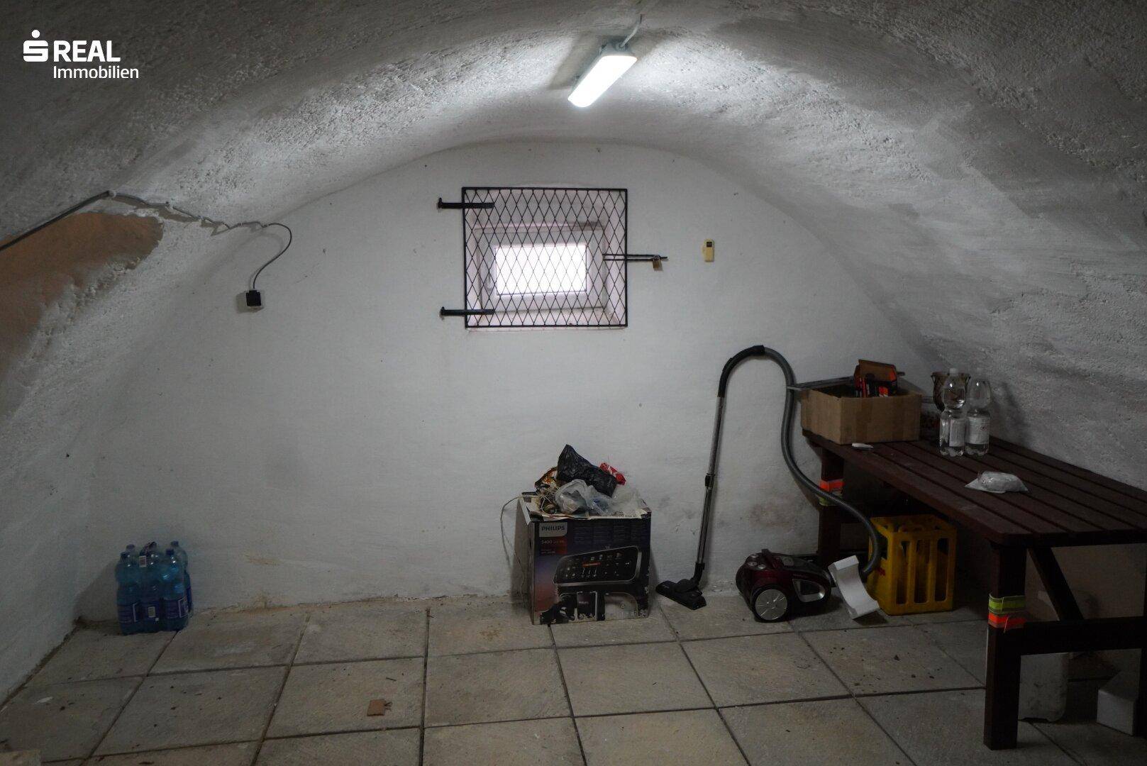 Geräumiger Gewölbekeller mit Fliesenboden, kleinem Fenster und Stauraum.