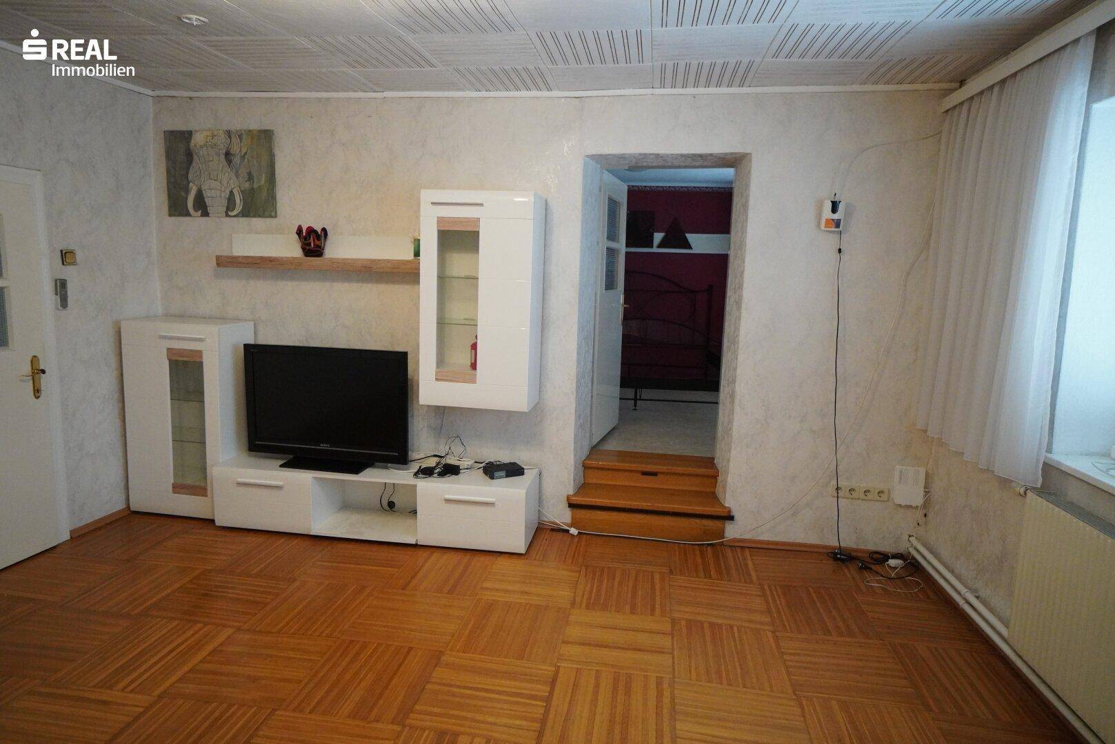 Wohnzimmer mit Parkettboden, moderner TV-Möbel und Zugang zu einem weiteren Raum.