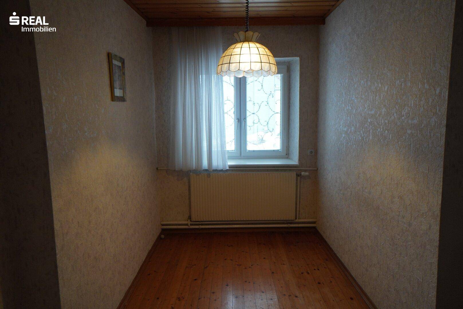 Kleiner Raum mit Holzdecke, Parkettboden und Fenster mit Vorhängen.