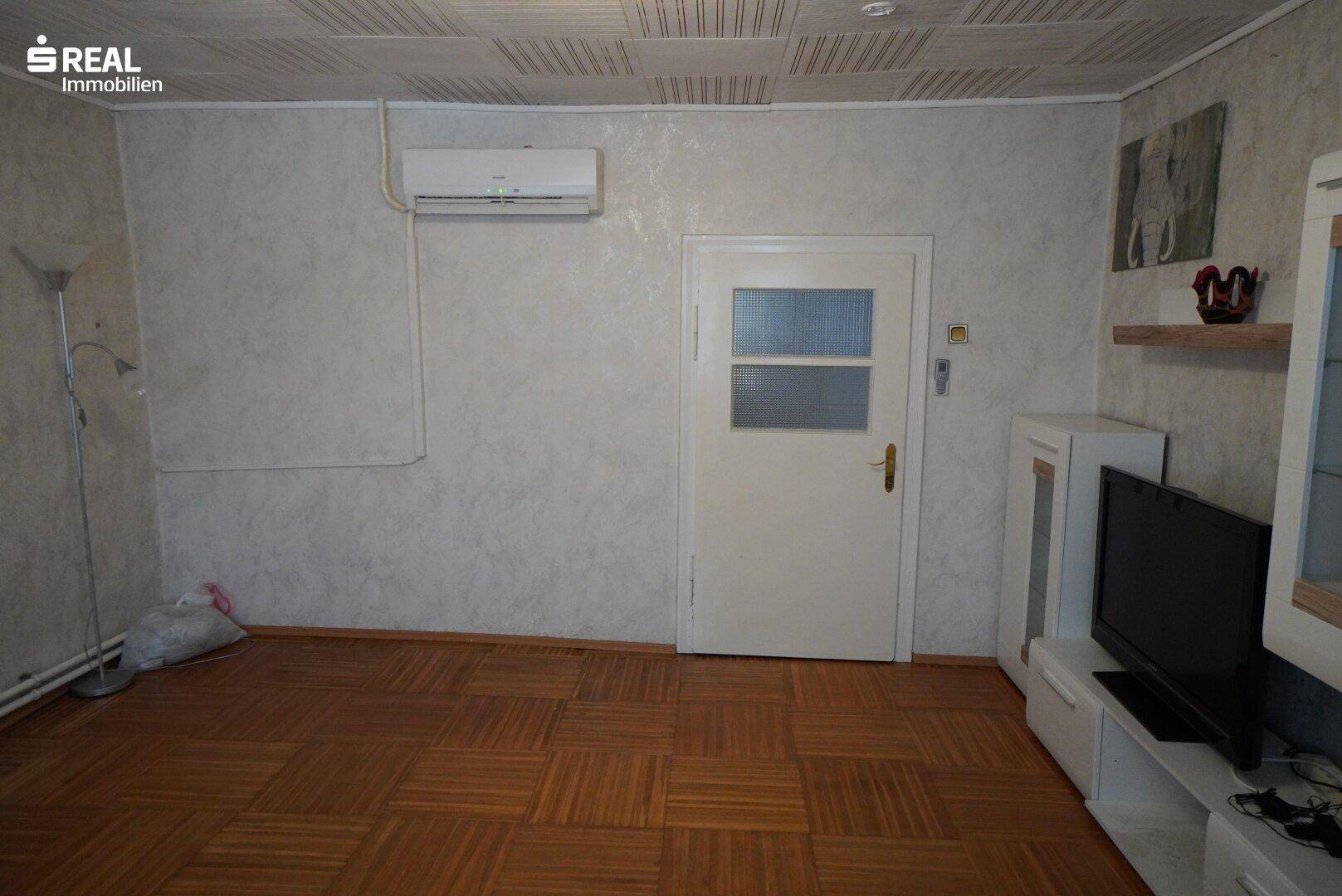 Wohnzimmer mit Parkettboden, Klimaanlage und weißer Tür.