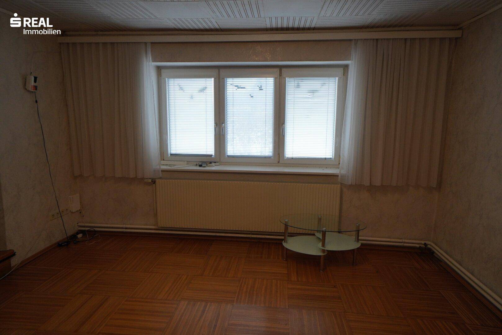 Helles Wohnzimmer mit Parkettboden und großen Fenstern, die viel Tageslicht hereinlassen.