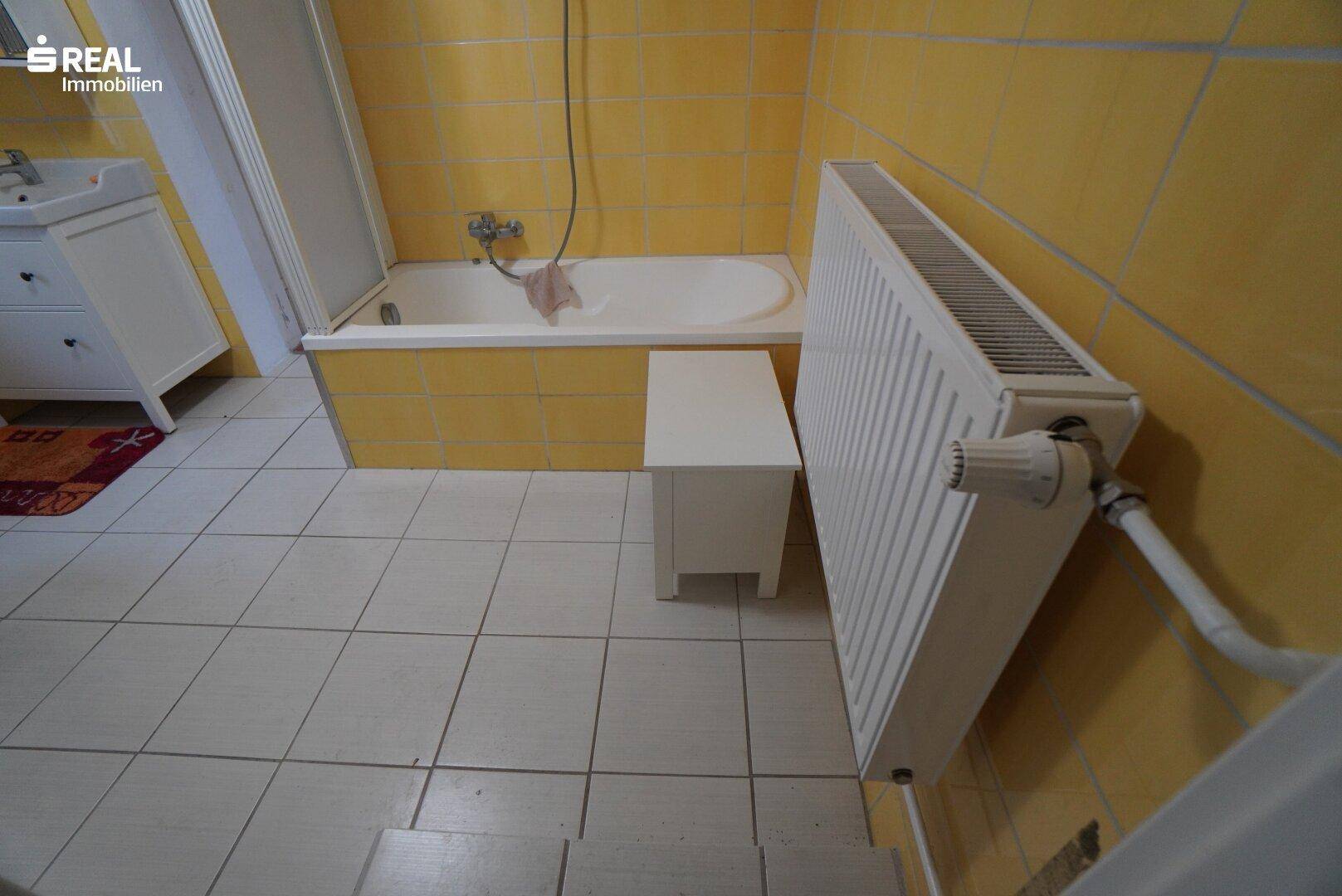 Badezimmer mit gelben Fliesen, Badewanne und Heizkörper.