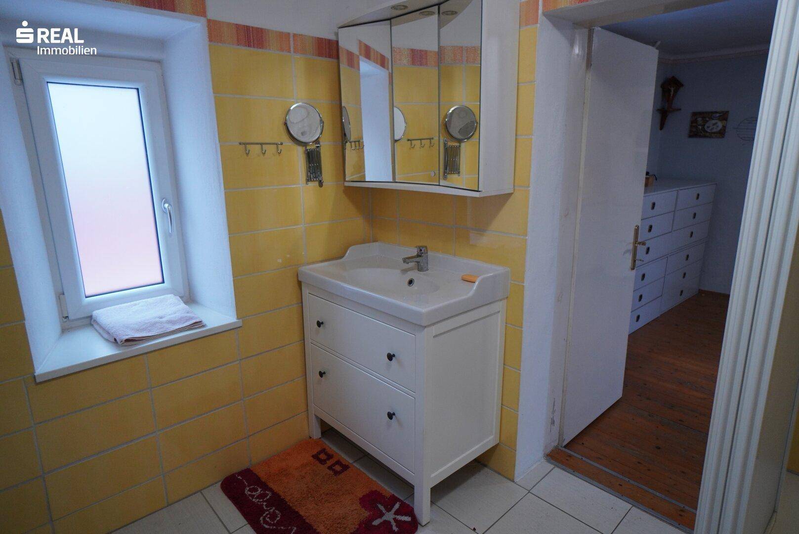 Badezimmer mit gelben Fliesen, Waschtisch, Spiegelschrank und Fenster.