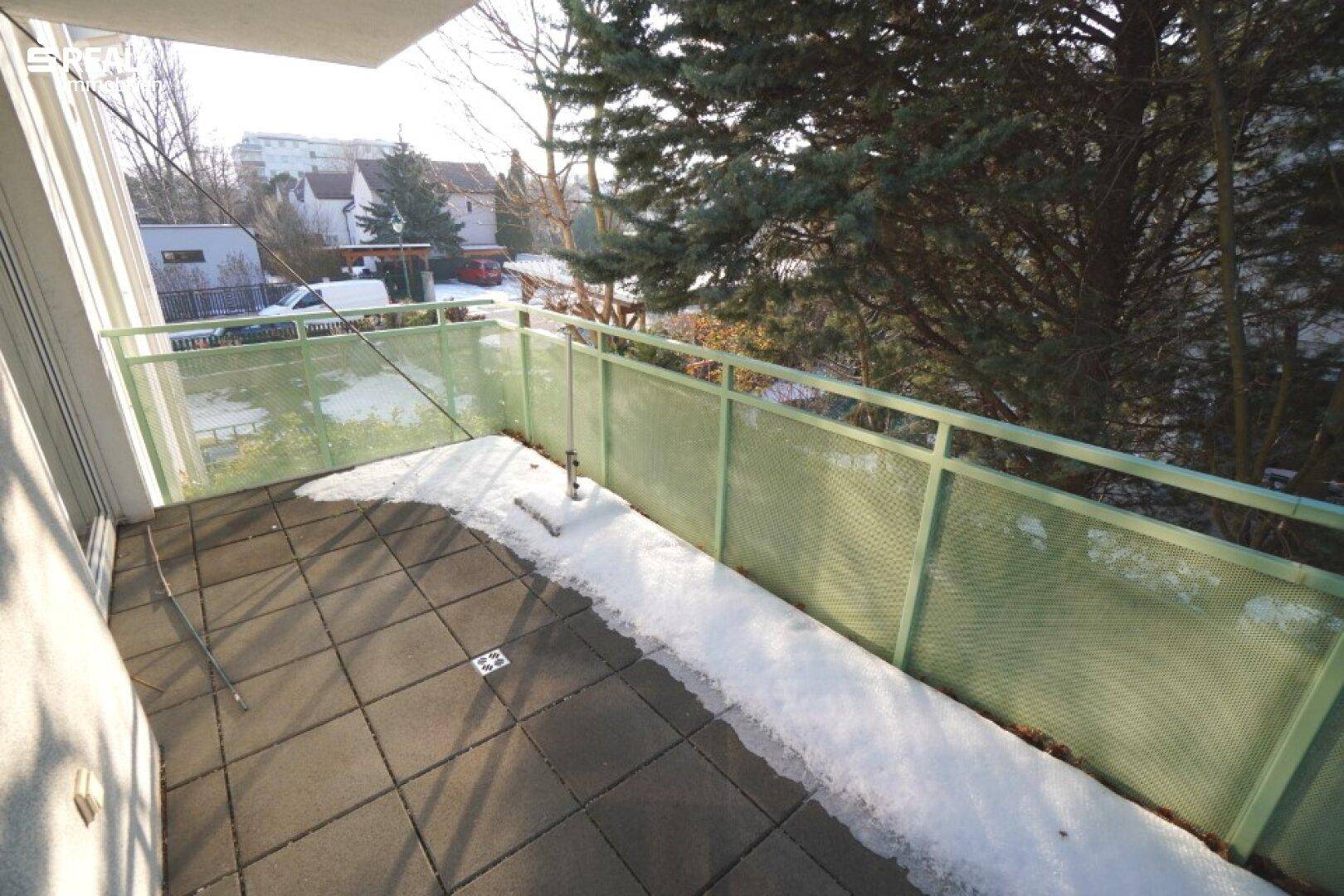 Gefliester Balkon mit grüner Brüstung und Blick ins Grüne, teilweise mit Schnee bedeckt.