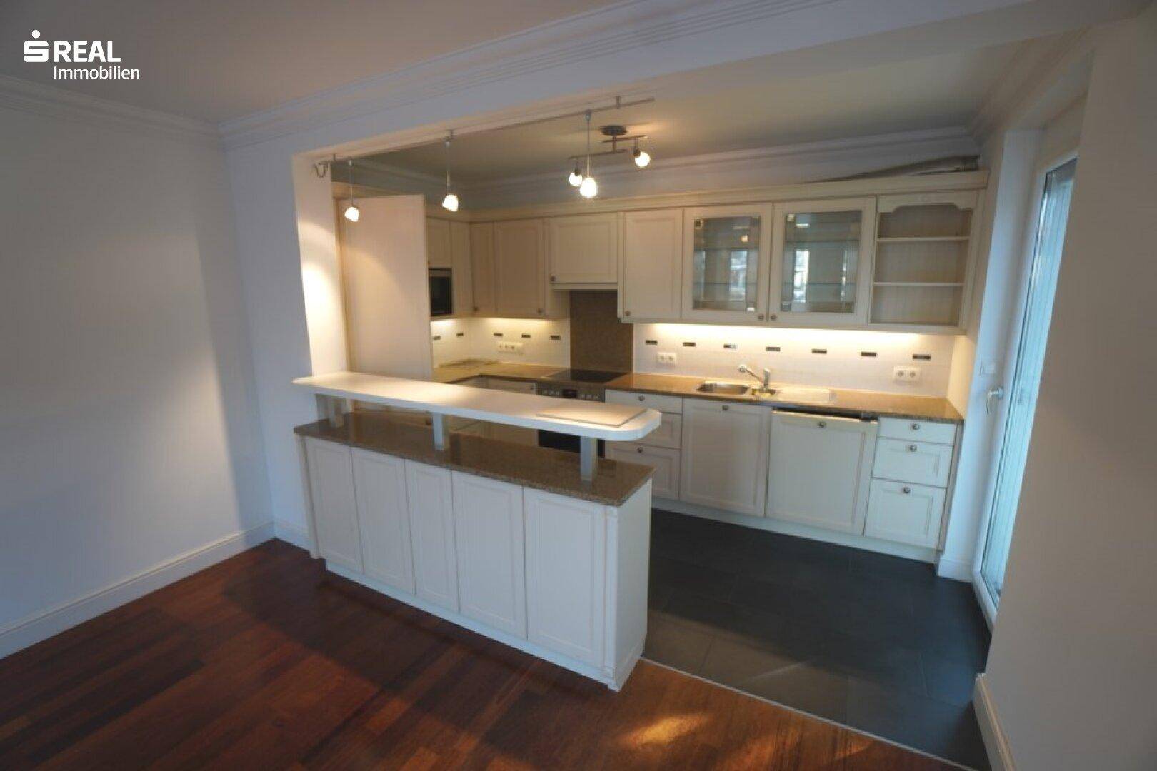 Helle Einbauküche mit Frühstücksbar, dunklen Arbeitsplatten und modernen Einbaugeräten.