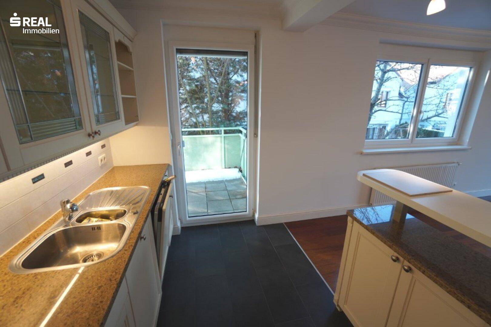 Küchenbereich mit Doppelspüle, Granitarbeitsplatte und direktem Zugang zu einem Balkon.