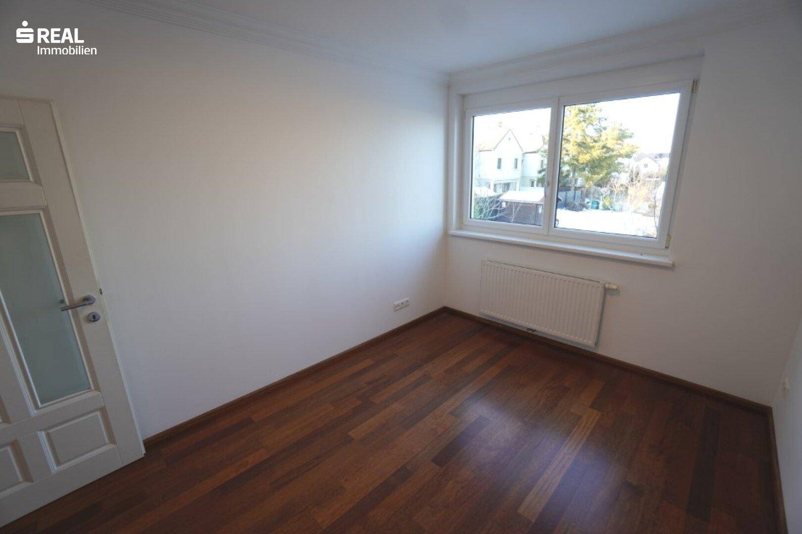 Geräumiges Schlafzimmer mit Hartholzboden und großem Fenster, das viel Tageslicht bietet.