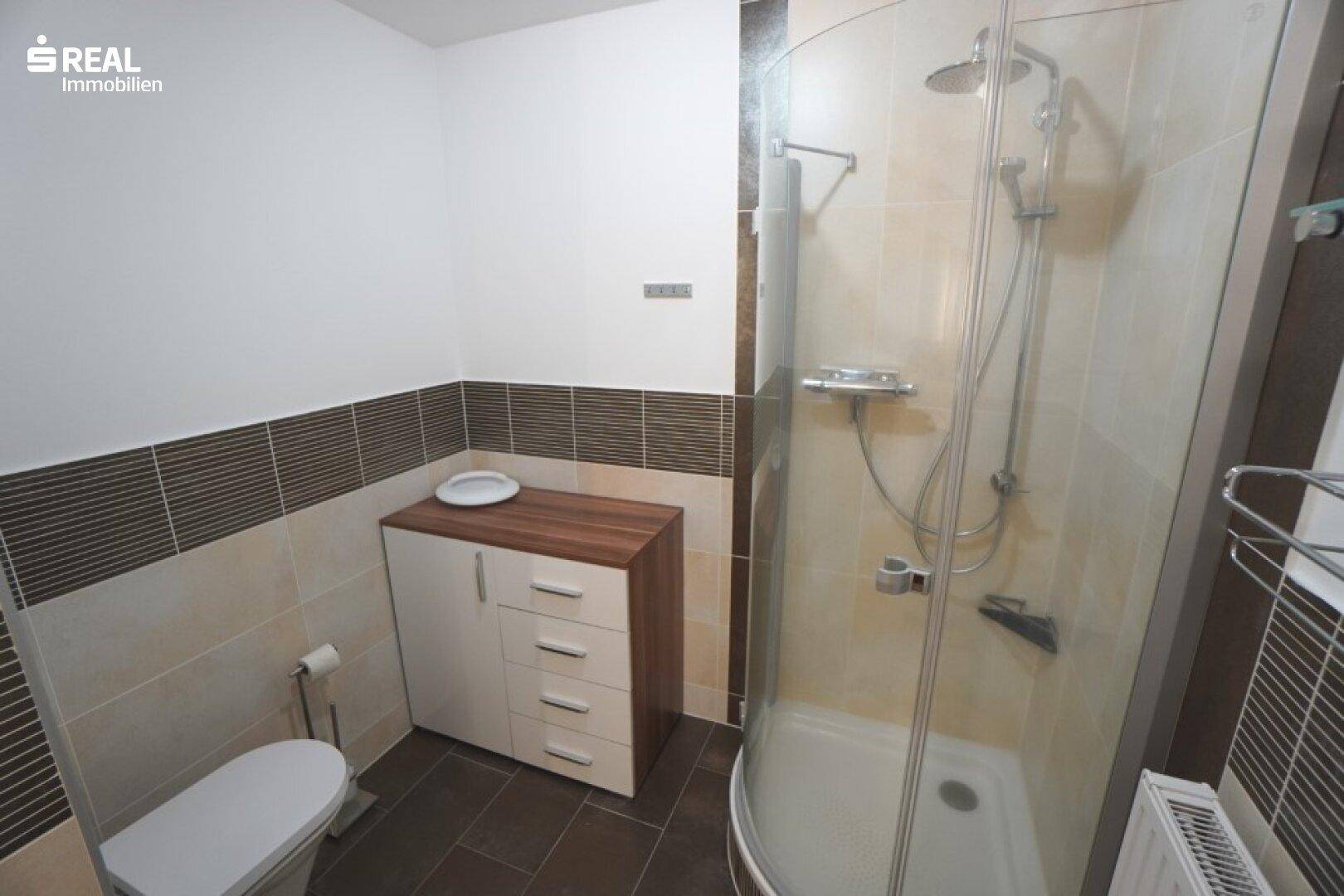 Badezimmer mit Duschkabine, WC und hellen Fliesen an Wänden und Boden.