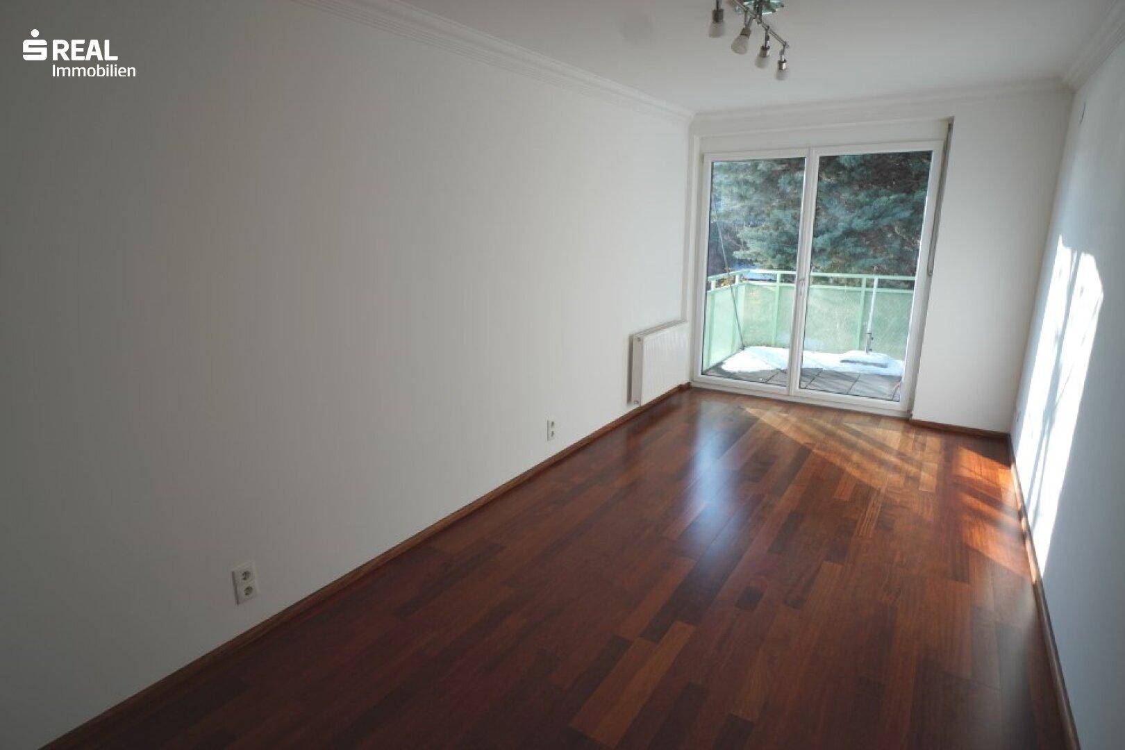Schlafzimmer mit dunklem Hartholzboden und breiter Schiebetür, die zu einem Balkon führt.