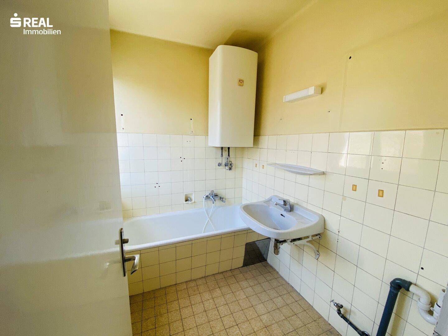 Veraltetes Badezimmer mit Badewanne, Waschbecken und gelblichen Fliesen, das eine Modernisierung benötigt.
