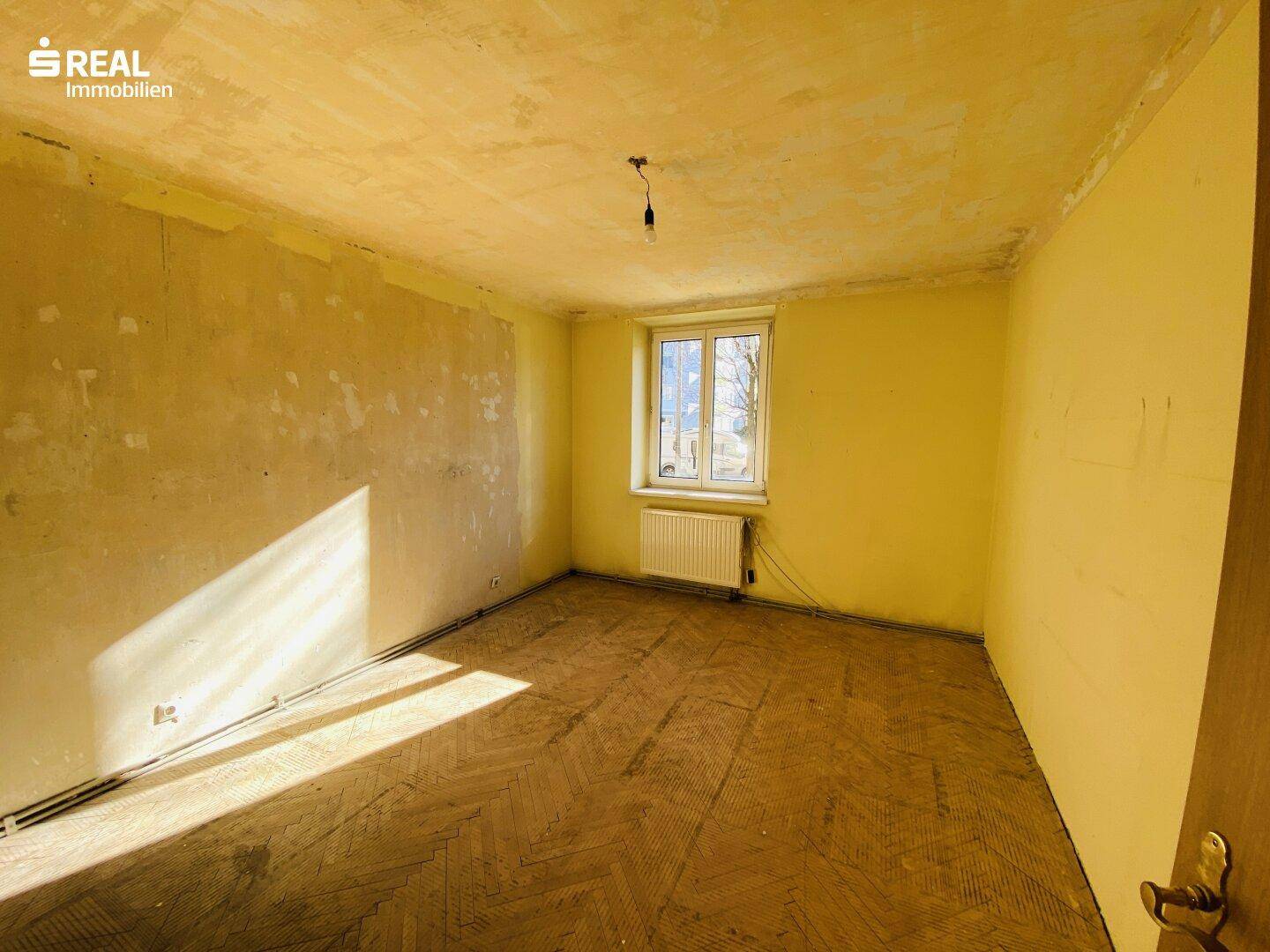 Geräumiges Zimmer mit einem Fenster und altem Parkettboden, ideal zur Neugestaltung.