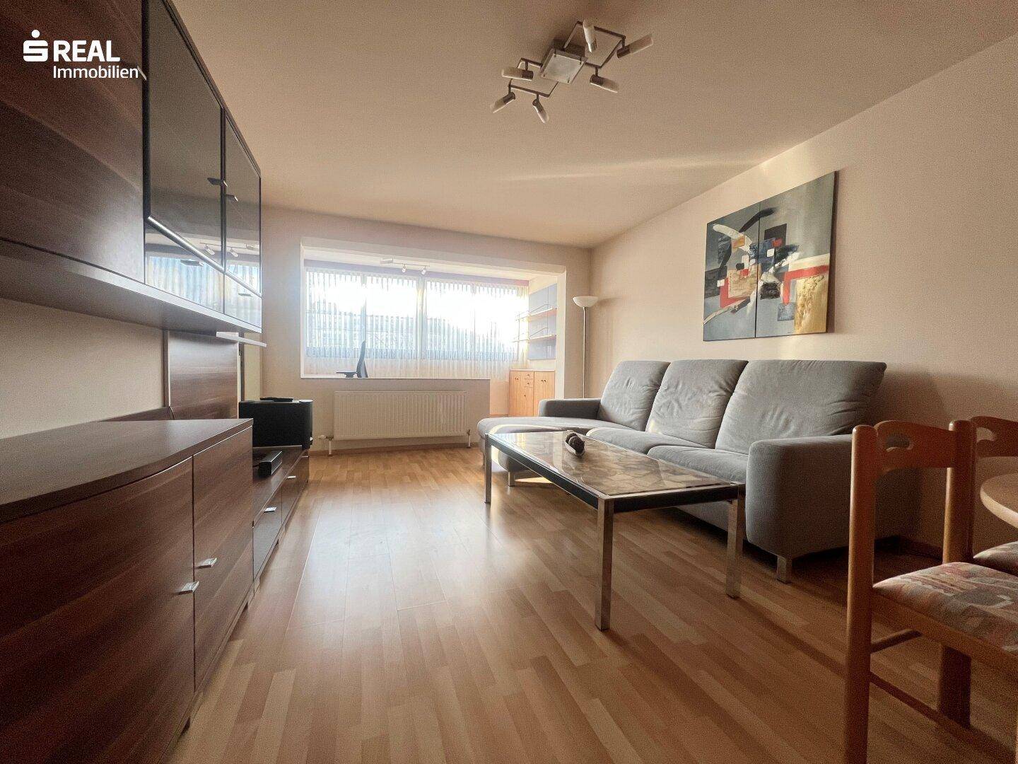 Helles Wohnzimmer mit großem Fenster, bequemer Couch und Holzmöbeln, ideal zum Entspannen.
