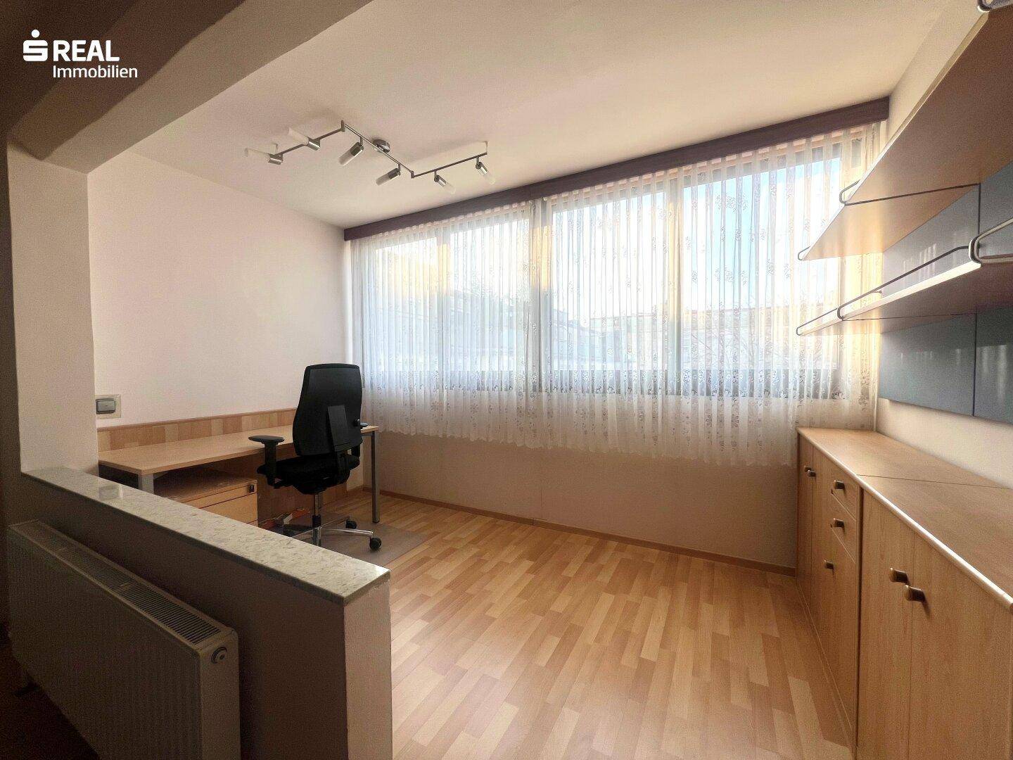 Heller Arbeitsbereich mit großem Fenster, Schreibtisch und praktischen Einbauschränken.