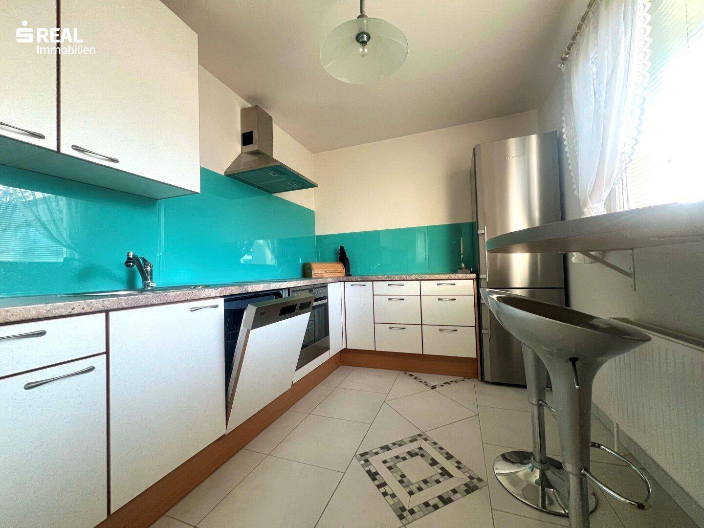 Moderne Küche mit weißen Schränken, türkiser Rückwand, Edelstahlgeräten und Frühstücksbar.