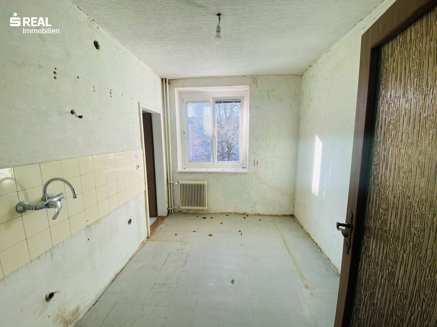 Leere Küche mit Fliesenboden und Fenster, bereit für eine neue Einrichtung.
