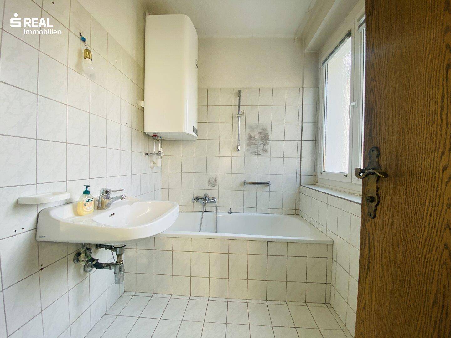 Badezimmer mit Badewanne, Waschbecken und Fenster, in einfachem Zustand.