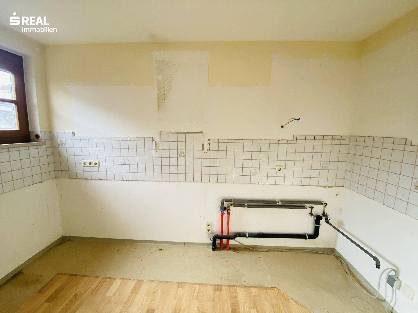 Leere Küche mit gefliestem Fliesenspiegel und sichtbaren Anschlüssen, bereit für eine neue Einrichtung.