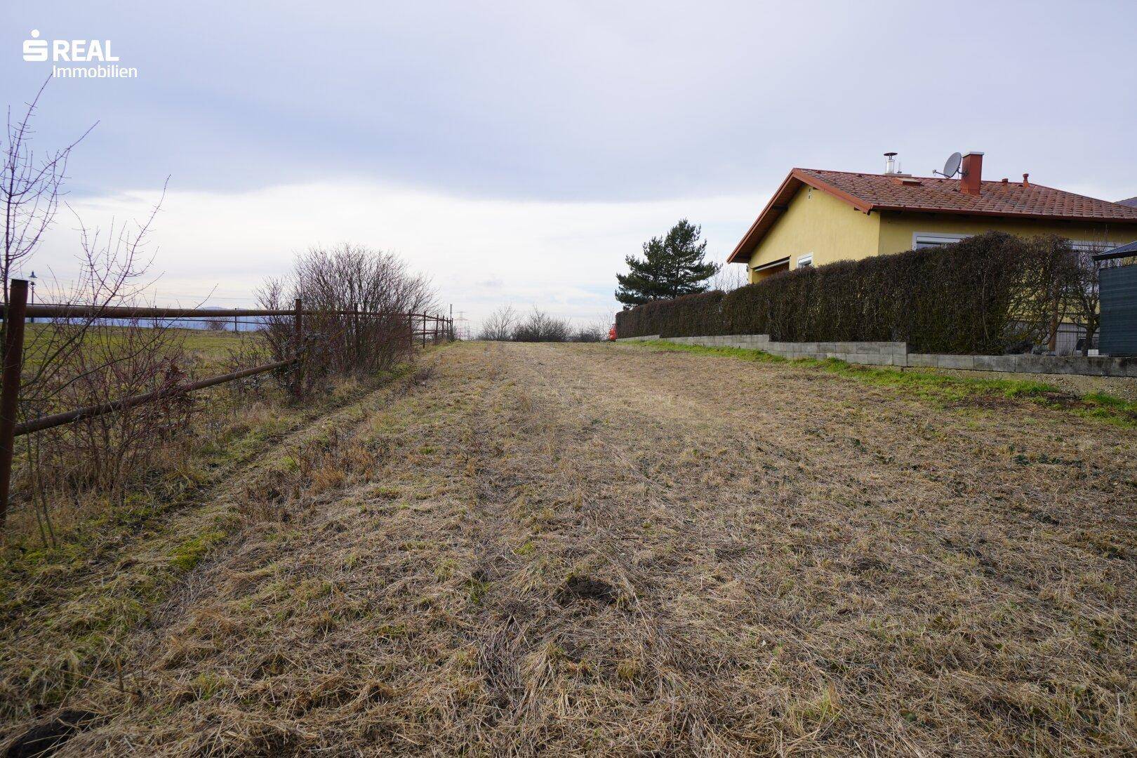Großes unbebautes Grundstück mit Blick auf die hügelige Landschaft und ein benachbartes Gebäude.