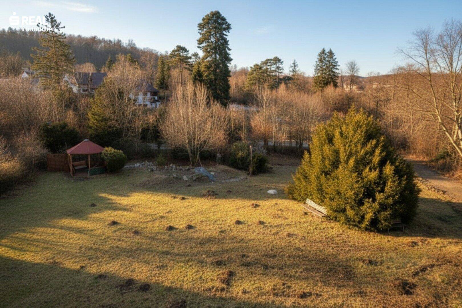 Weitläufiger Garten mit Pavillon und Bäumen, beleuchtet von der tiefstehenden Abendsonne.