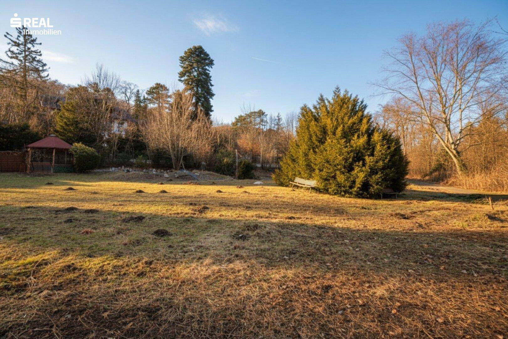 Großer Gartenbereich mit Rasenfläche, Bäumen und einem Gartenpavillon unter blauem Himmel.