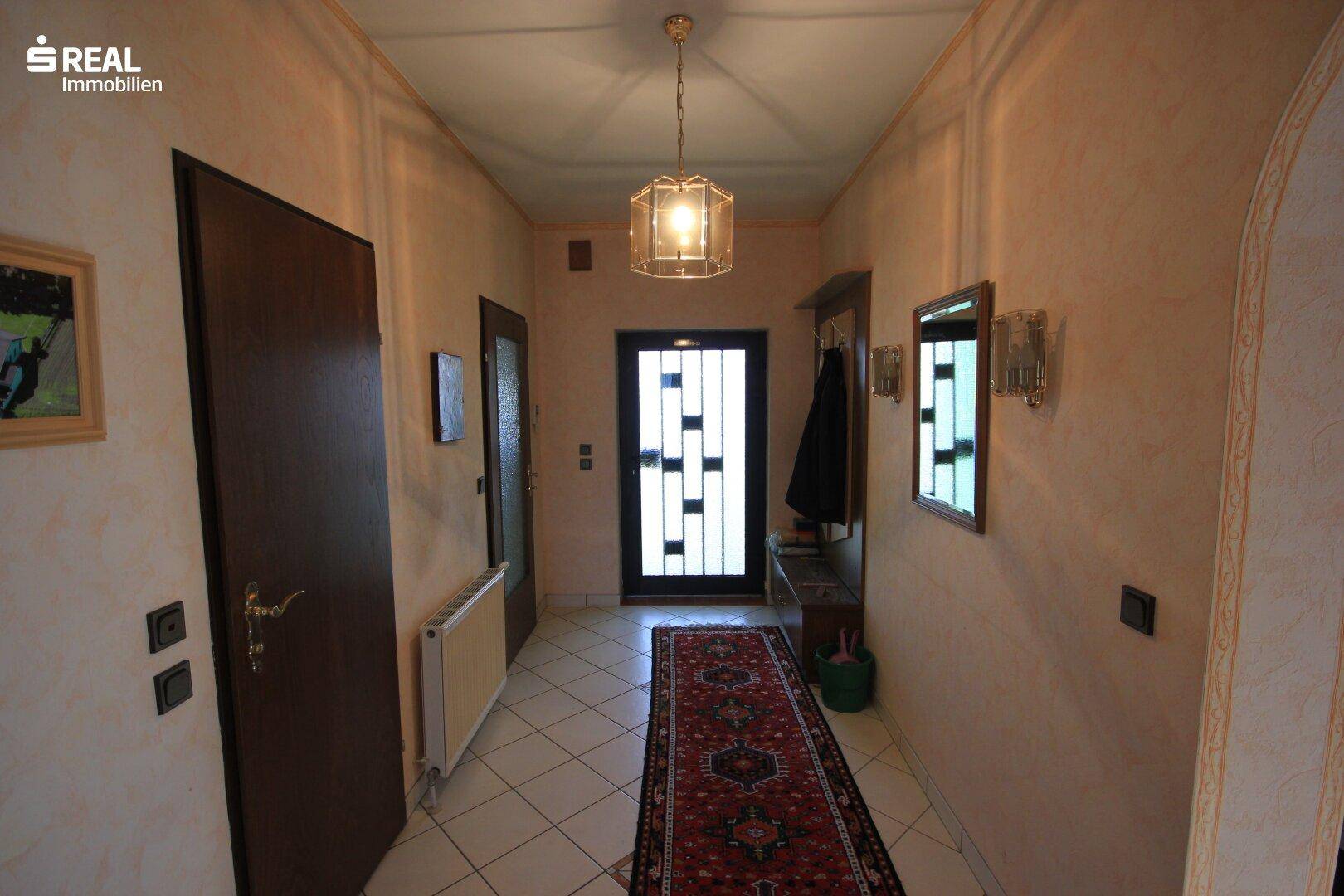 Eingangsbereich des Hauses mit Fliesenboden, Garderobe und einer verzierten Eingangstür.