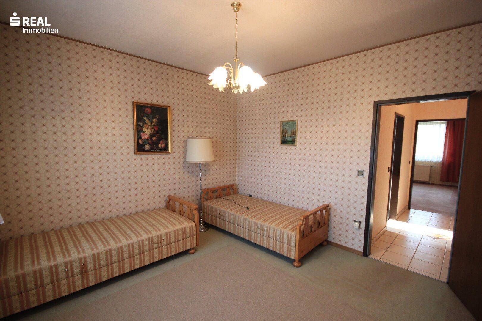 Schlafzimmer mit zwei Einzelbetten, Teppichboden und gemusterter Tapete.