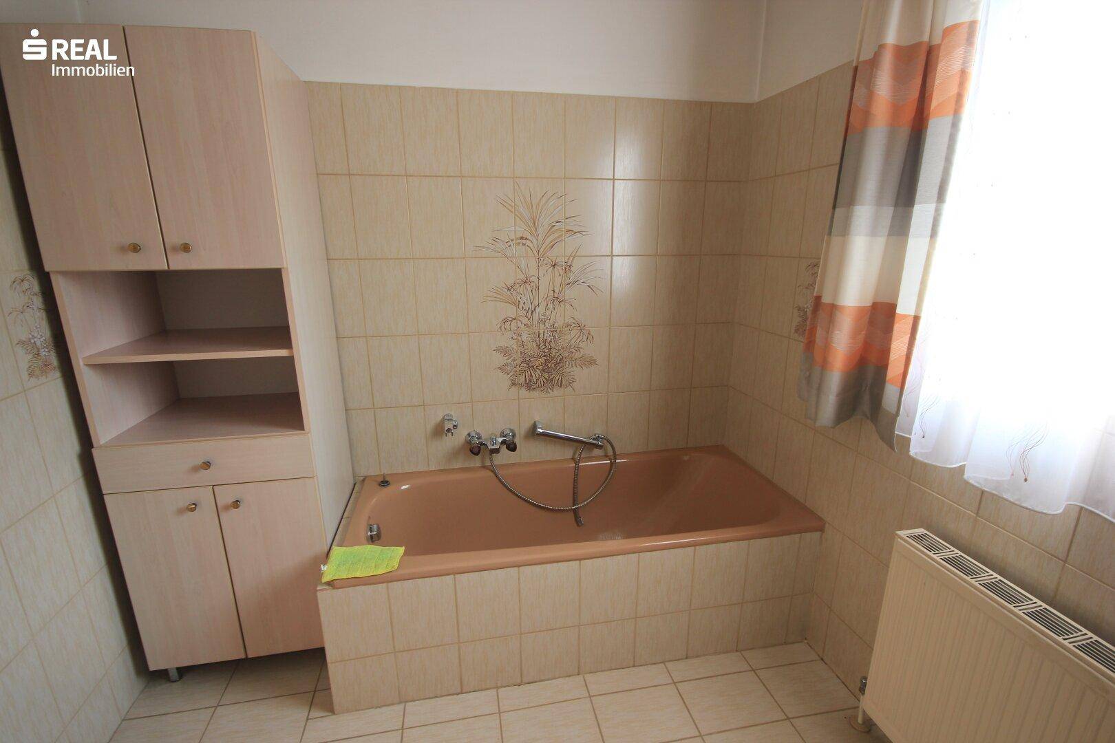 Badezimmer mit Badewanne, beigefarbenen Fliesen und einem Hochschrank.