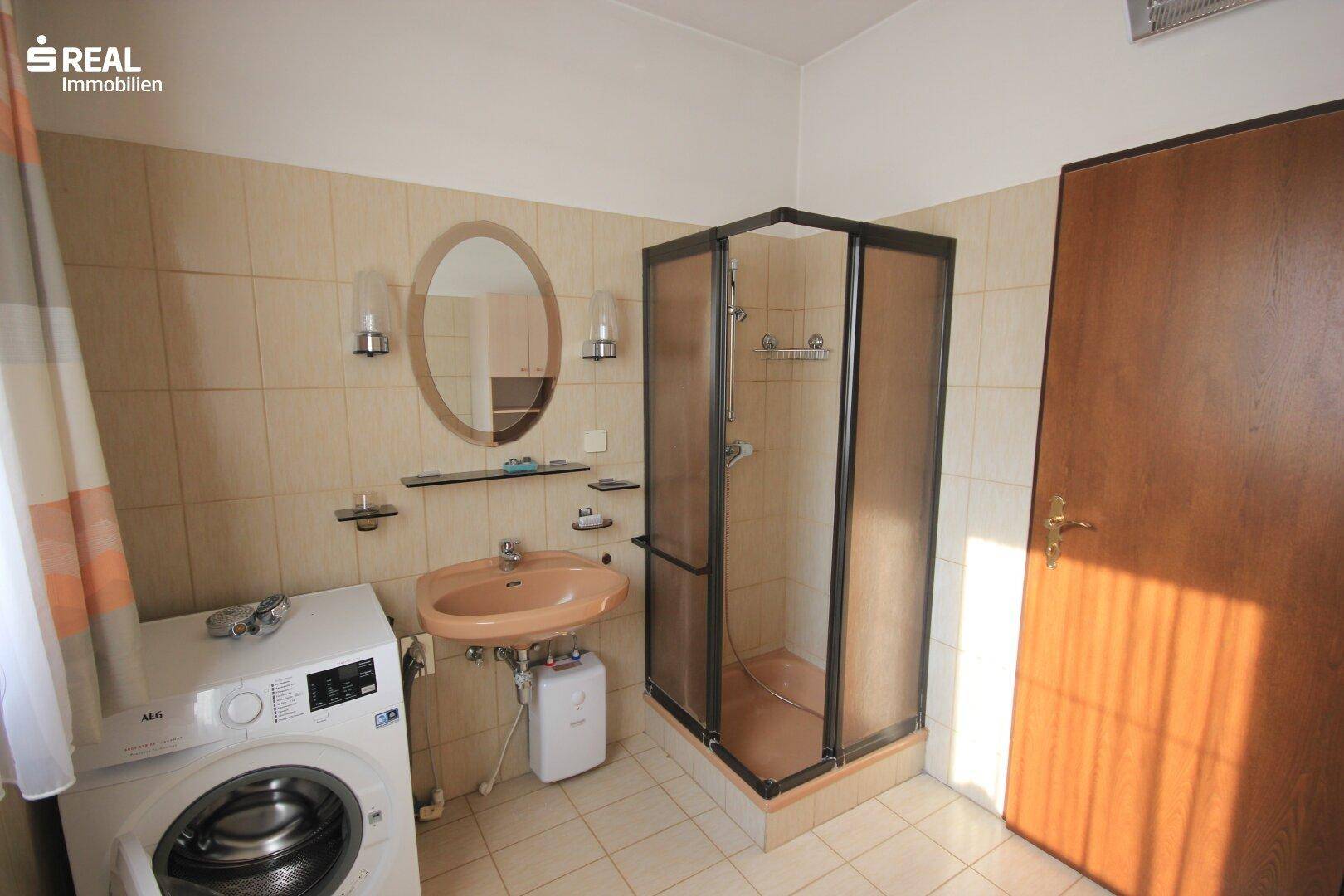 Badezimmer mit Dusche, Waschbecken, Spiegel und Waschmaschine.