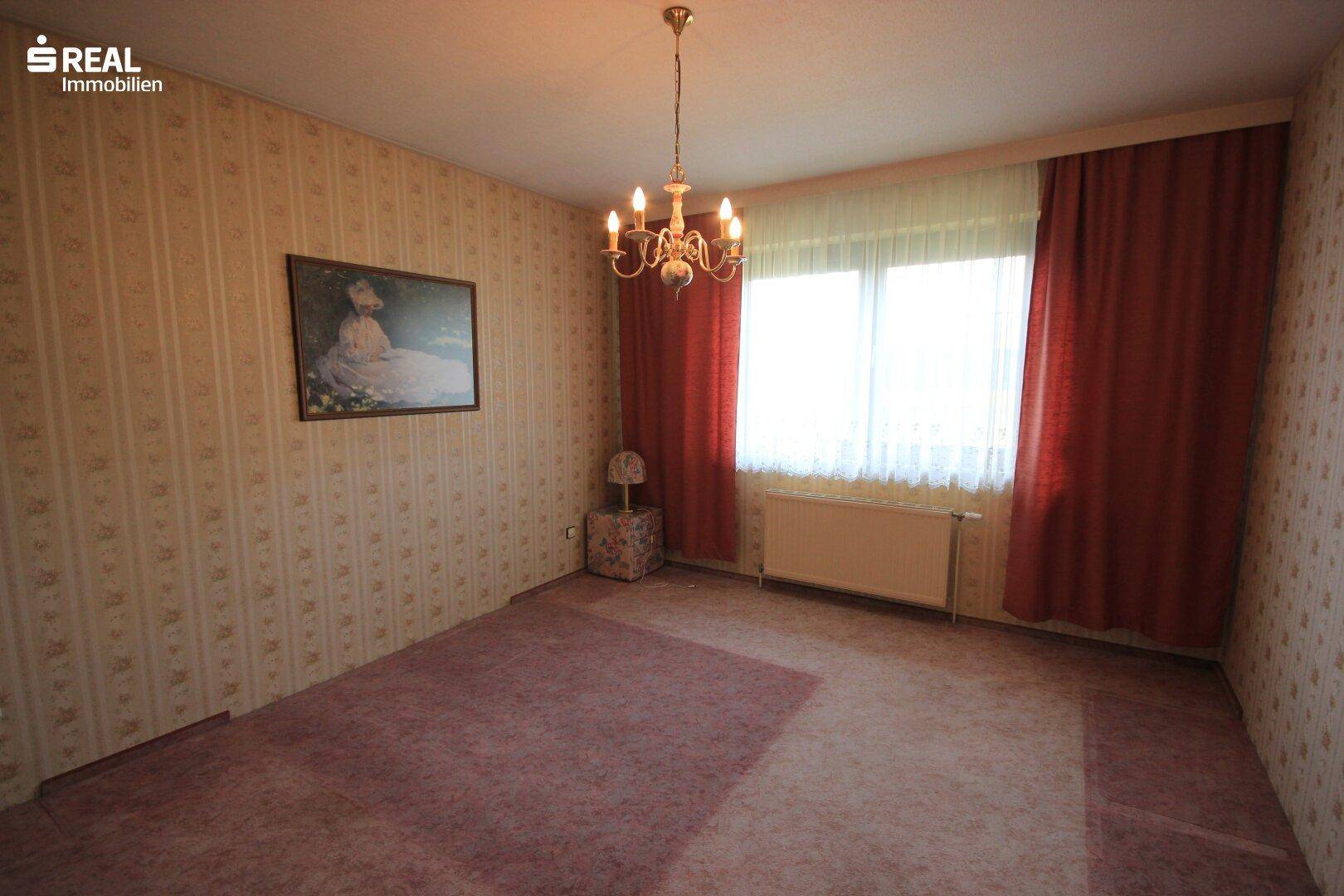 Schlafzimmer mit Teppichboden, Fenster und einem Kronleuchter an der Decke.