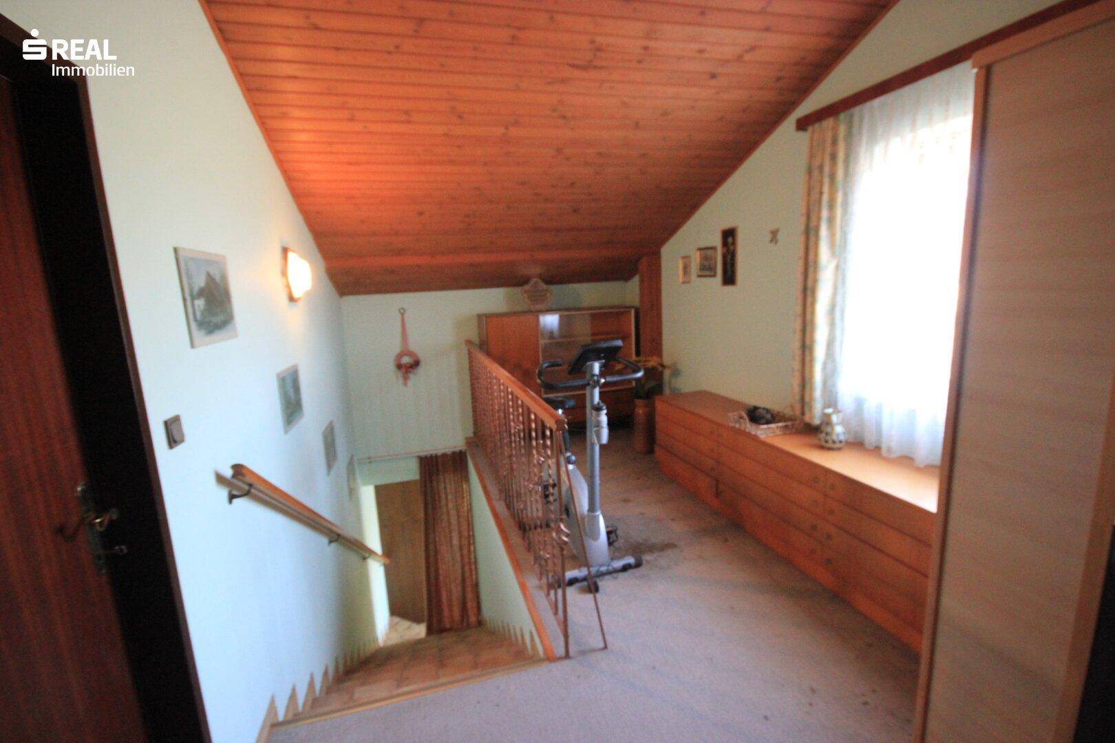Ausgebauter Dachbodenbereich mit Holzdecke, Treppenzugang und Fitnessgerät.