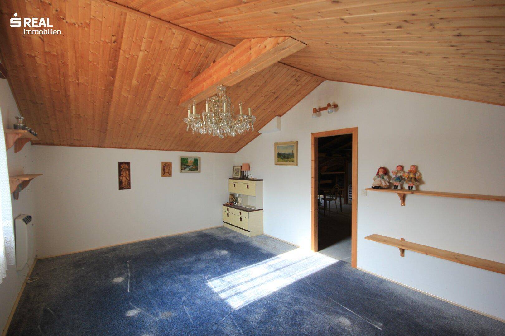 Heller Dachbodenraum mit Holzdecke, Teppichboden und einem Kronleuchter.