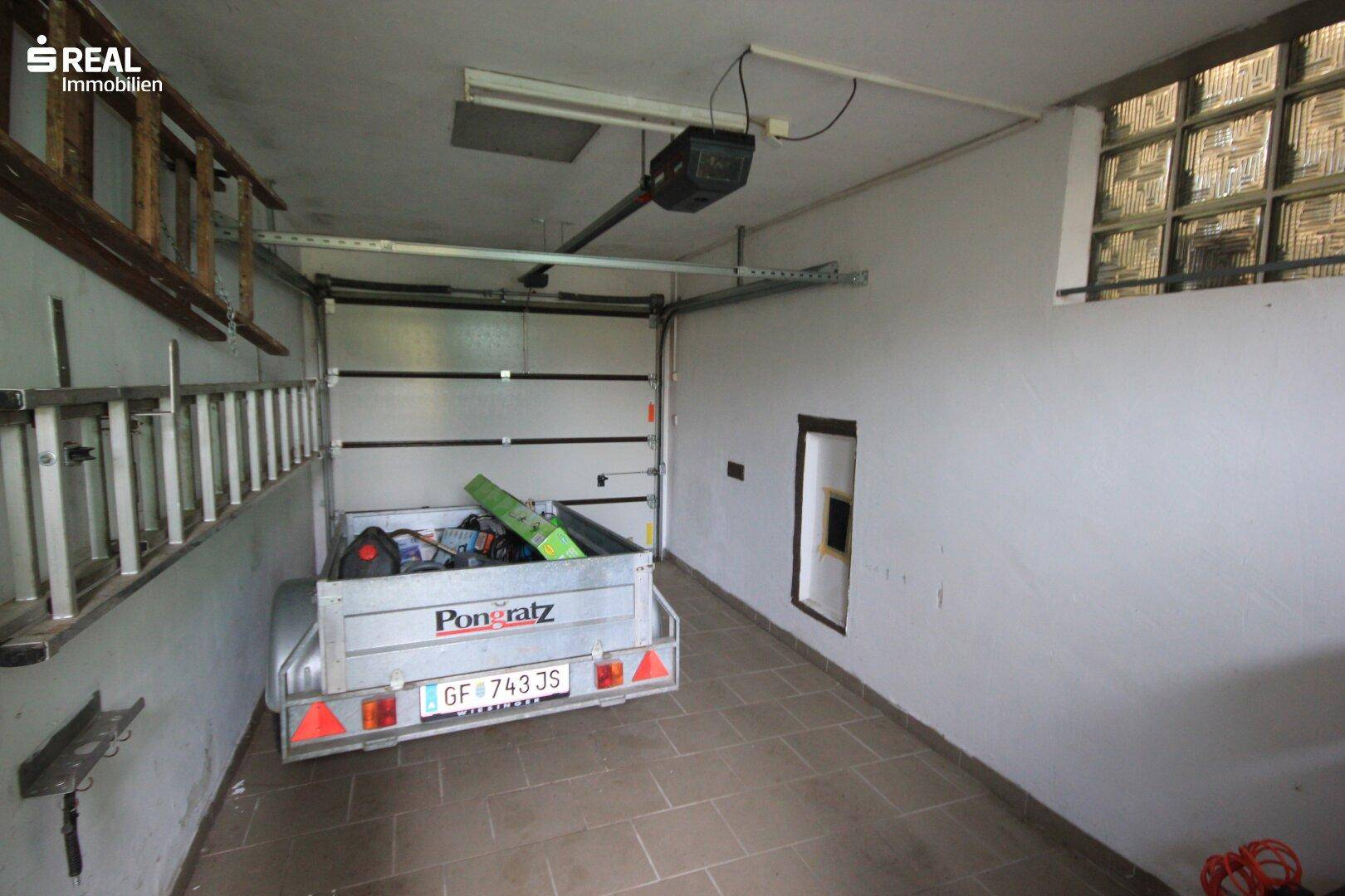 Garage mit Rolltor, Fliesenboden und Platz für ein Fahrzeug oder Lagerung.