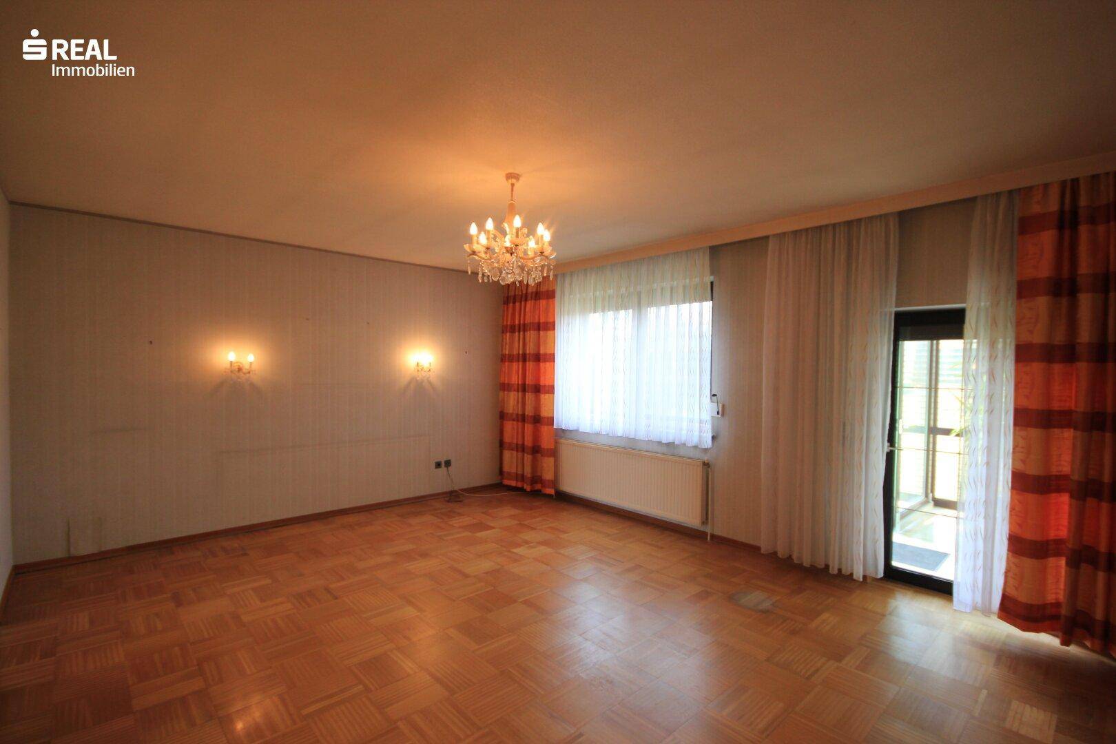 Geräumiges Wohnzimmer mit Parkettboden, Kronleuchter und Zugang zur Terrasse.
