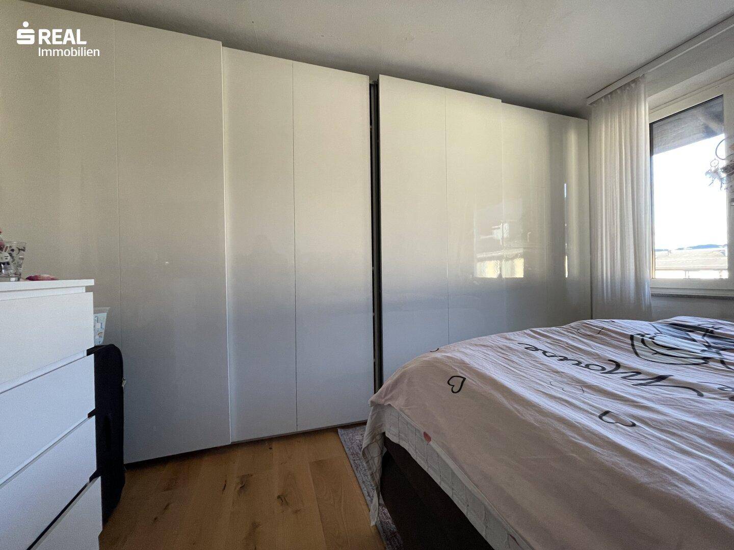 Schlafzimmer mit Holzboden, großen weißen Einbauschränken und Fenster.