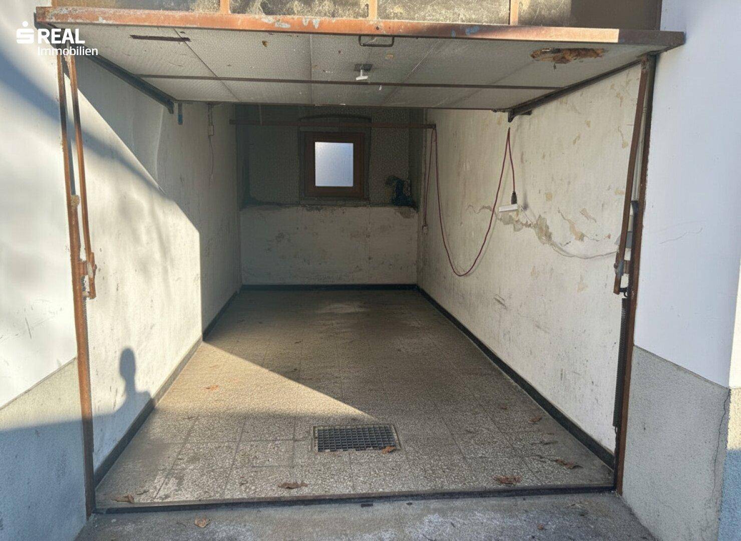 Leere Garage mit Betonboden, einem kleinen Fenster und sichtbaren Gebrauchsspuren an den Wänden.