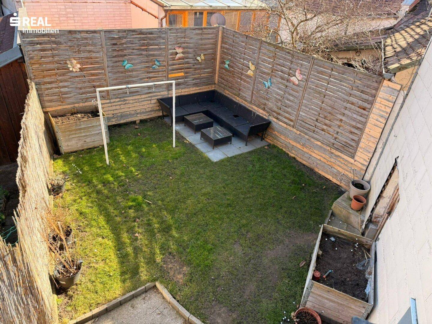 Kleiner Gartenbereich mit Rasen, einer Sitzecke und einem hohen Holzzaun für Privatsphäre.