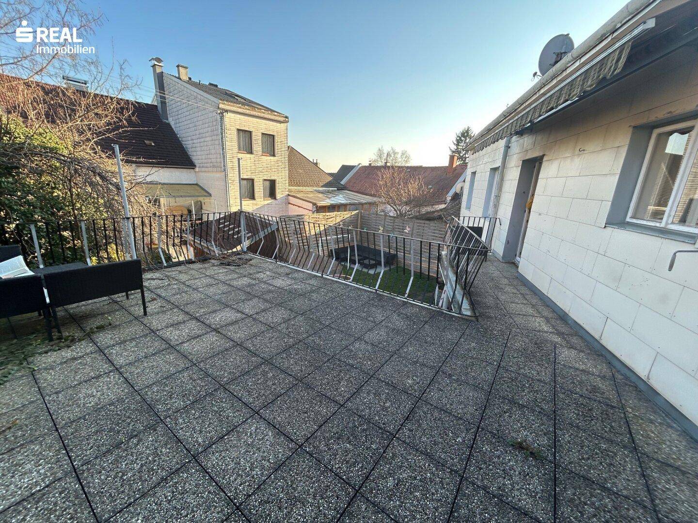 Große geflieste Terrasse mit Metallgeländer und Blick auf die umliegenden Gebäude und Gärten.