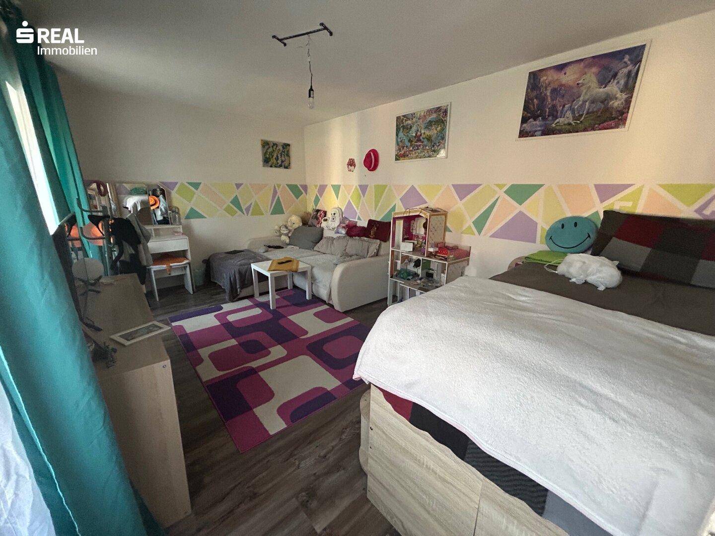 Kinderzimmer mit farbenfroher Wandgestaltung, einem Bett und einem Sofa, ideal zum Spielen.