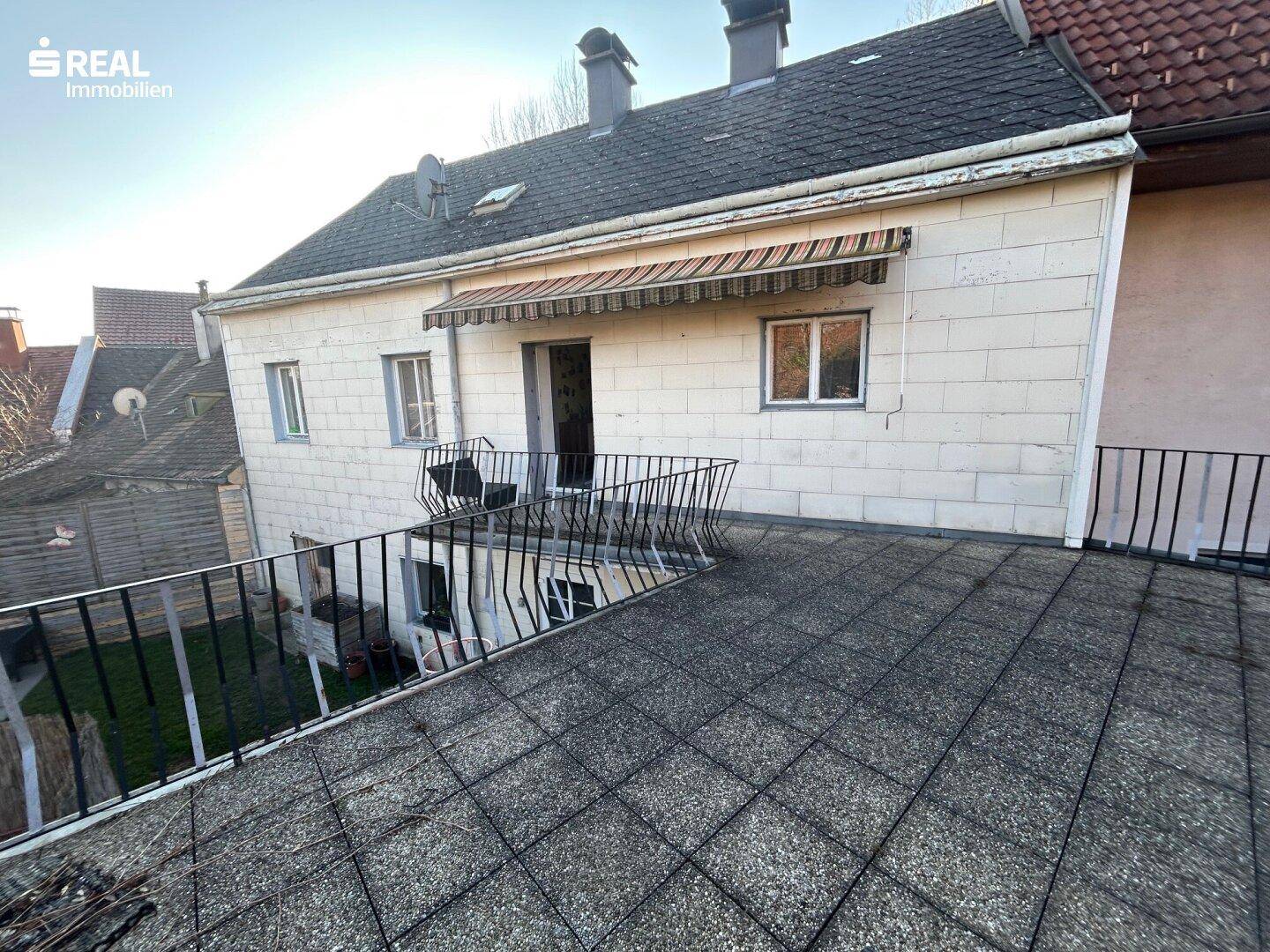 Blick von der Terrasse auf die Rückseite des Hauses mit Markise über einem Fenster und Tür.