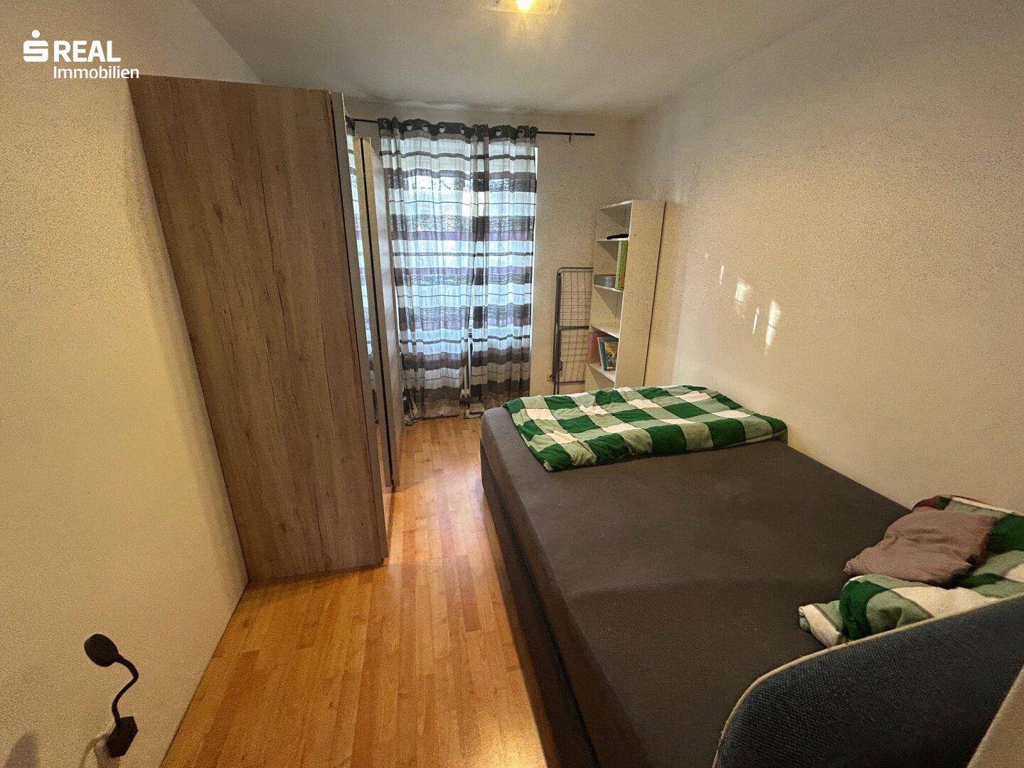 Gemütliches Schlafzimmer mit Einzelbett, Holzschrank und karierten Vorhängen am Fenster.